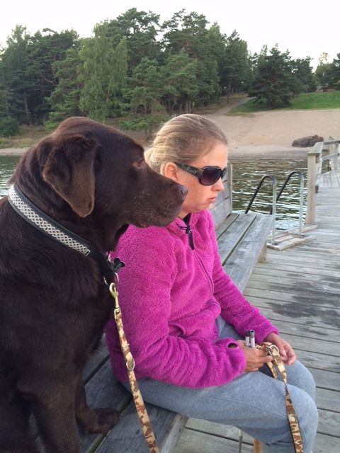 Jag och Duncan på bryggan. Jag har en rosa fleecejacka, solglasögon och håller i ett melerat koppel. Duncan, i brun päls tittar ut mot vattnet.