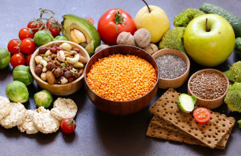 Urval av vegetarisk mat. Nötter, frön, frukt och grönsaker presenterade snyggt på ett mörkt bord