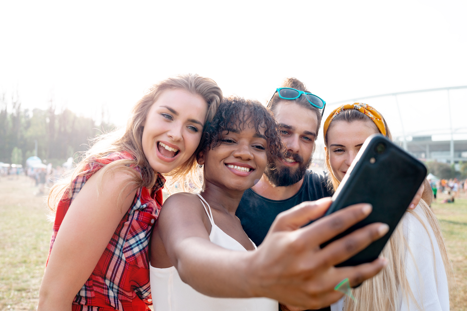 Ett kompisgäng på fyra personer tar ett gruppfot till sociala medier utomhus på en strand. Gruppen består av tre tjejer och en kille med varierande etnisk bakgrund.