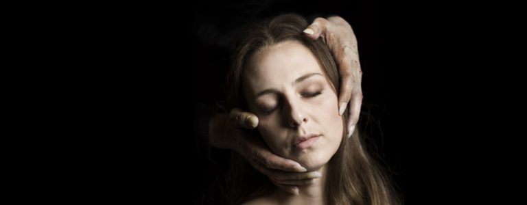 Pressbild från "Dom blinda". Ett ansikte med en kvinna som blundar. Runt ansiktet ser man två händer mot en svart bakgrund.