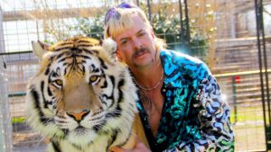 Bild på Joe Exotic intill en tiger med stängsel bakom.