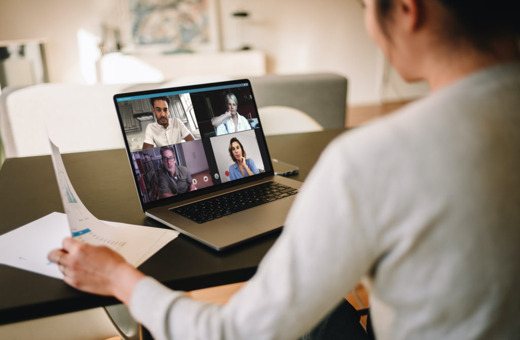 Tjej klädd i ljus tröja och mörkt hår sitter framför dator. På skärmen syns fyra ansikten som deltar i ett videomöte.